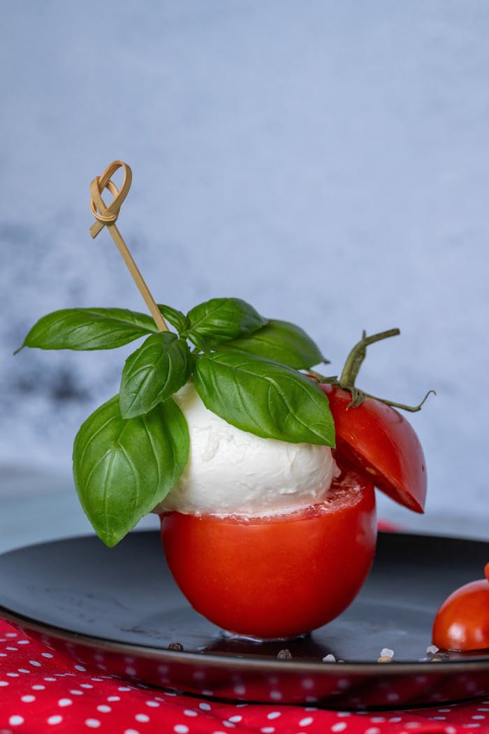 Caprese salad with fresh basil leaves, ripe tomato, and mozzarella on a black plate, perfect for summer meals.